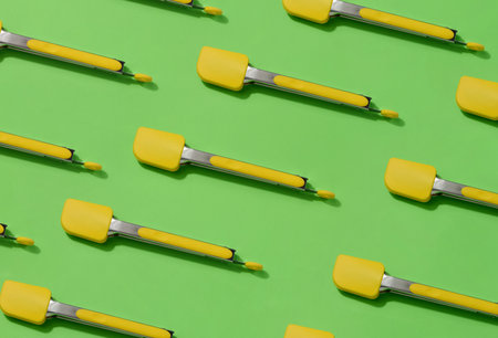 Yellow kitchen tongs with shadow on green background, patternの写真素材