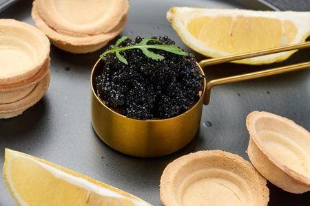 Black sturgeon caviar in copper bowl, lemon wedges and empty tartlets on table, close upの写真素材