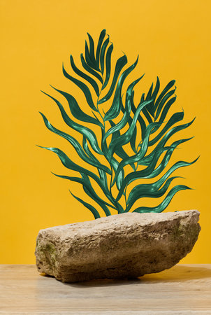 Stone on yellow background with green branch, stage for cosmetics and products demonstration, copy spaceの写真素材