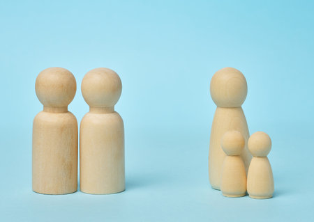 Wooden dolls symbolize different family models. One group represents a couple, while the other represents a single parent with two children on a blue backgroundの写真素材