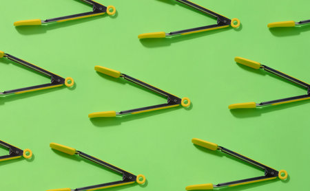 Yellow kitchen tongs with shadow on green background, pattern. Top viewの写真素材
