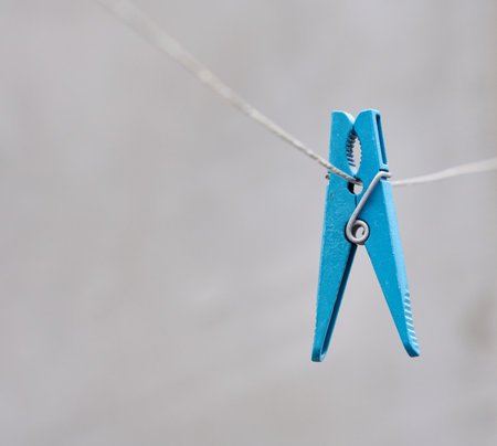 A blue plastic clothespin hangs on a clotheslineの写真素材