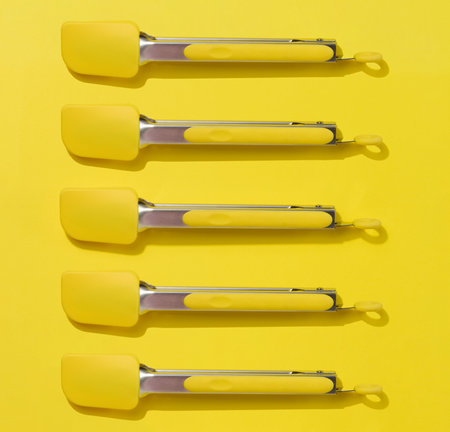 Yellow kitchen tongs with shadow on yellow background, top viewの写真素材