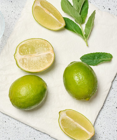 A minimalist composition featuring green whole limes and a juicy halved lime paired with a tied...