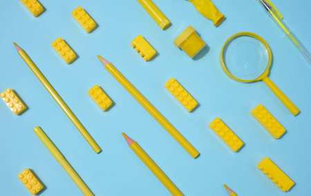 Various yellow objects including pencils, magnifying glass and toy blocks scattered on blue background, top viewの写真素材