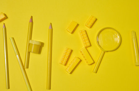 Collection of yellow stationery, building brick, and magnifying glass on a yellow background....