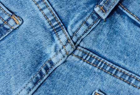 Close-up of blue denim jeans fabric showing reinforced cross-stitching. Detailed view of the seam and textile texture for design and quality themesの写真素材