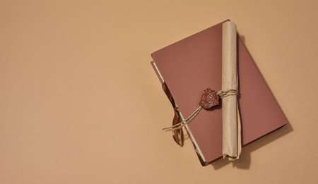 A closed book with a sealed scroll lying on top, on a neutral background.の写真素材