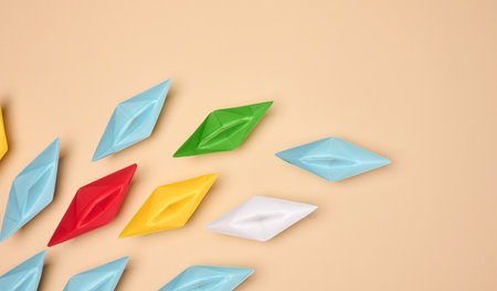 Multicolored origami paper boats are placed on a beige background, symbolizing diversityの写真素材