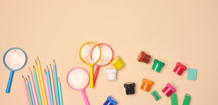A collection of brightly colored school and office supplies, including pencils, magnifying glasses, paper clips and erasers, scattered on a neutral backgroundの写真素材