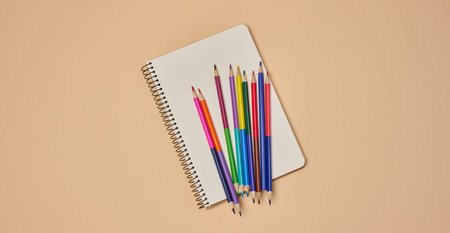 Top view of an open notebook with colorful pencils on a beige background. Flat lay composition of...