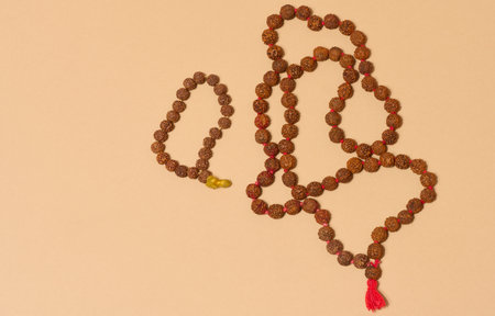 Top view of two strands of rudraksha beads, one of which is longer and has a red tassel, placed on a...