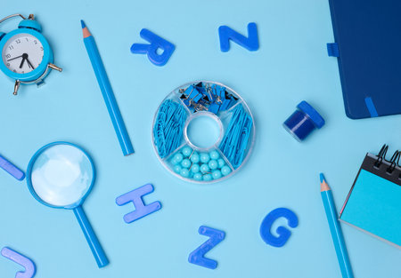Flat lay of blue stationery, learning items letters, magnifying glass, supplies, and an alarm clock...