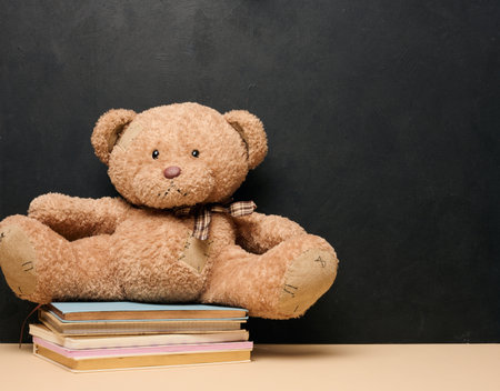 Brown teddy bear sitting on a stack of colorful books symbolizing childhood, studying or reading, on a black background with space for textの写真素材