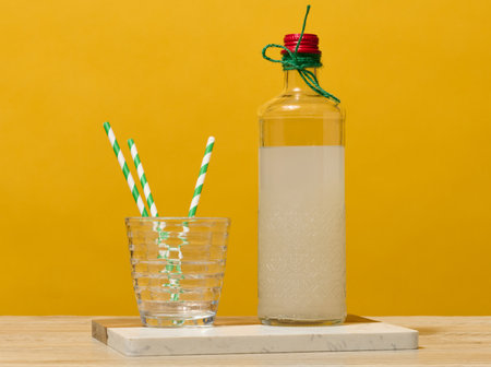 A transparent glass bottle of lemonade stands next to a faceted glass containing three green striped straws.の写真素材