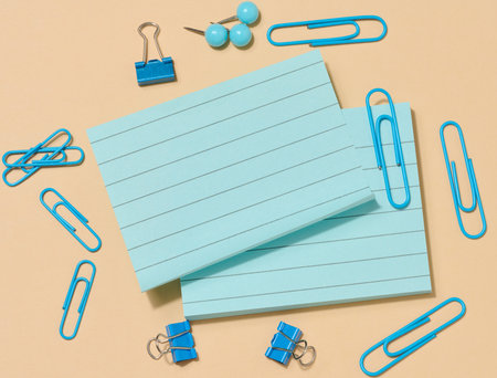 Several stacks of light blue sticky notes and many blue paper clips of various shapes, arranged on a beige background. Top viewの写真素材