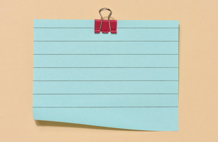 Blue sticky note secured with a red paper clip, centered on a beige background. Top view.の写真素材