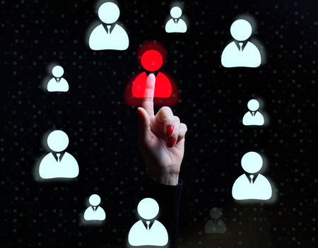 Female hand pointing at one red highlighted user icon among many blue icons on black background, recruitment conceptの写真素材