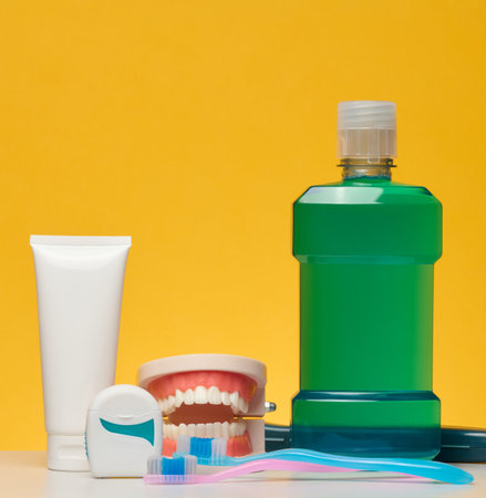 Oral hygiene kit including a tube of white toothpaste, dental floss, a green bottle of mouthwash and two toothbrushes, on a yellow backgroundの写真素材
