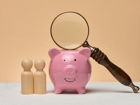 Piggy bank, wooden human figures, above the piggy bank there is a magnifying glass. The composition symbolizes financial analysis, investments or search for funds.の写真素材