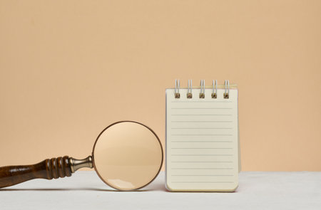 An open notebook with blank lined sheets of paper and a magnifying glass next to it. Searching for...