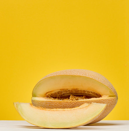 Half of a cantaloupe melon and a single slice placed on a white surface. Yellow background.