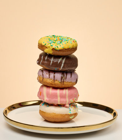 Stack of donuts with different toppings and glazes on round plate, beige backgroundの写真素材