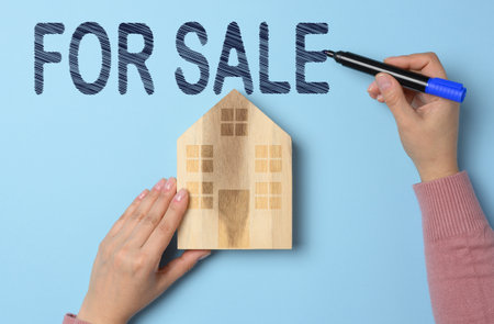 Wooden house and for sale sign on blue background. Conceptual image on real estate sale.の写真素材