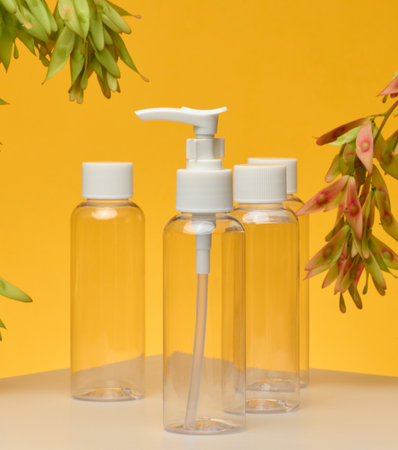 Transparent cosmetic bottles with white caps pump, flip-top. Yellow background, branches with green seeds hanging from the top.の写真素材