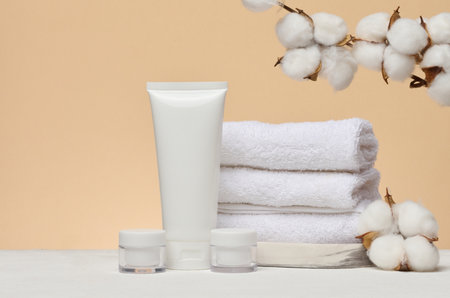 Stack of white towels and white plastic tubes and jars with cosmetics on beige backgroundの写真素材