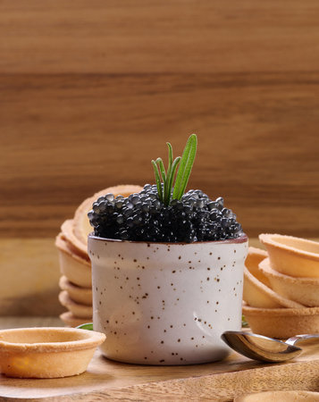 Black caviar in mini tartlet on wooden board, ceramic pot with caviar and stacks of empty tartlets.Wooden backgroundの写真素材
