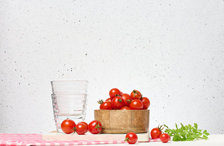 Wooden bowl with red ripe cherry tomatoes and empty glasses on white backgroundの写真素材