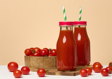 Glass bottles with tomato juice with red caps. Fresh red tomatoes lie on a wooden stand and in front of themの写真素材