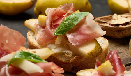 Italian bruschetta with prosciutto, pear slices, cream cheese and fresh basil, garnished with sesame seedsの写真素材