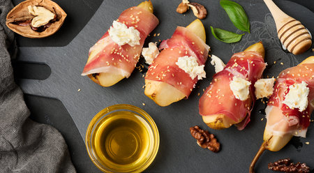 Sliced ââpear wrapped in prosciutto, topped with cream cheese and sesame seeds, served on an elegant black slab plate, top viewの写真素材
