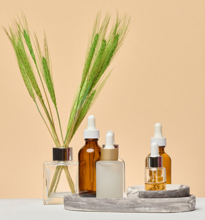 Various glass bottles with pipettes containing cosmetic serums or oils are arranged on a marble stand. Beige backgroundの写真素材