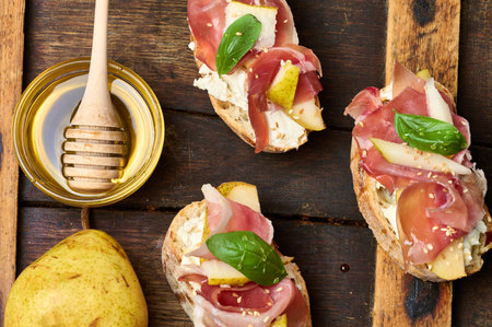 Italian bruschetta with prosciutto, pear slices, cream cheese and fresh basil, garnished with sesame...