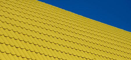 A section of a bright yellow corrugated roof, photographed at an angle against a clear blue sky.の写真素材