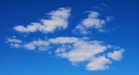 Several small cumulus clouds with soft white edges hovering against a clear, rich blue sky
