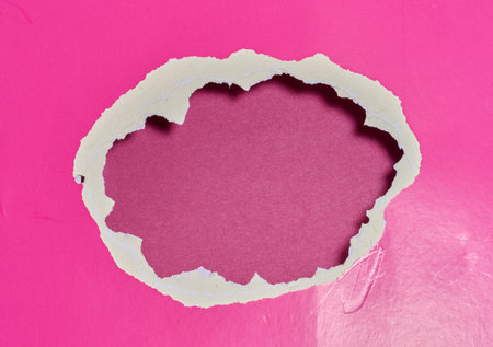 A jagged, round hole in a sheet of bright pink glossy paperの写真素材