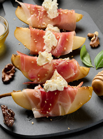 A close-up of an appetizer of pear, prosciutto and cream cheese topped with walnuts and honeyの写真素材