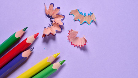 Multicolored wooden pencils and shavings on a violet background, top view