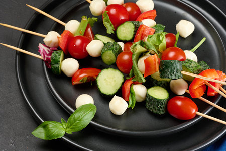 Appetizer of fresh vegetables and cheese on wooden skewers in a plateの写真素材
