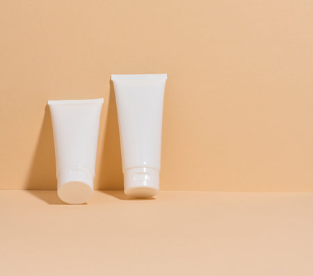 Two white cosmetic tubes without markings on a minimalist beige background.の写真素材