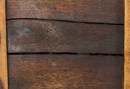 The texture of an old, darkened wooden board with deep horizontal cracks and scuffs. The frame is made of light-colored wooden planks on the sides.の写真素材