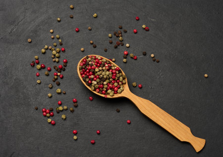 Mixed dry peppercorns in a wooden spoon on a black table, top viewの写真素材