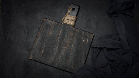 A vintage black cutting board with a handle tied with twine and dark cheesecloth on a black textured background. Blank space for text.の写真素材