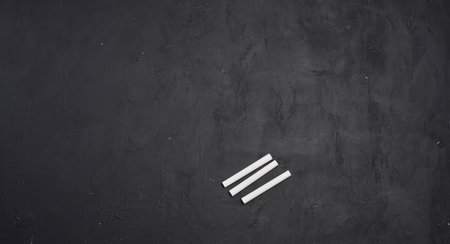 An empty black chalkboard and white chalk. Space for writing.