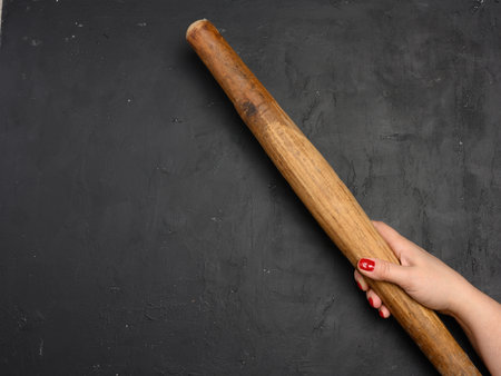 Female hand holding a vertical antique wooden rolling pin against a black background. Baking and cooking conceptの写真素材