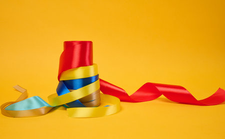 Rolled bright satin ribbons on a yellow background, festive decorの写真素材